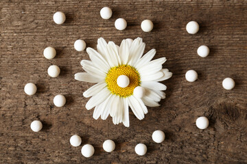 Fototapeta premium Homeopathic remedy and chamomile flower on wooden background, flat lay