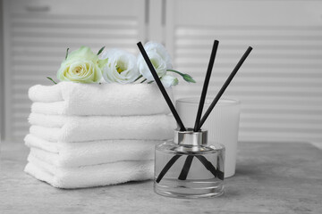 Towels, reed air freshener, scented candle and flowers on grey table indoors