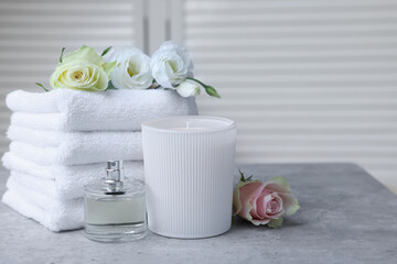 Towels, bottle of perfume, scented candle and flowers on grey table indoors