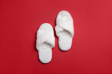 Pair of soft white slippers on red background, top view