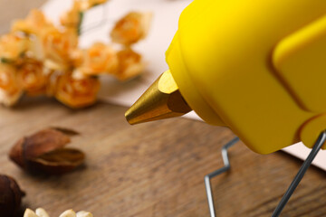 Hot glue gun with handicraft materials on wooden table, closeup