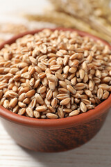 Wheat grains in bowl on white wooden table, closeup