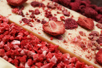 White chocolate bar with freeze dried strawberries as background, closeup