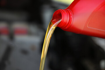 Naklejka premium Pouring motor oil from red container against blurred background, closeup