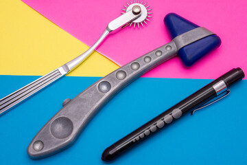 Neurological diagnostic tools: hammer, flashlight for checking pupillary response to light, Wartenberg wheel or neurowheel lie on abstract pink, yellow and blue background. Photo for use in neurology 