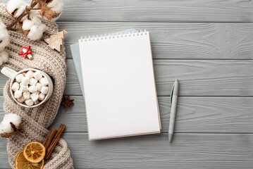 Winter concept. Top view photo of open reminder pen cup of cocoa with marshmallow cotton branch knitted scarf dried orange slices anise cinnamon sticks on grey wooden table background with empty space