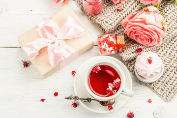 Obraz na płótnie Canvas The concept of romantic tea. Wrapped gift, hibiscus tea, a bouquet of delicate roses, sweets