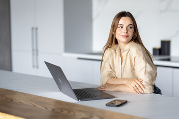 Happy young woman using laptop in the kitchen