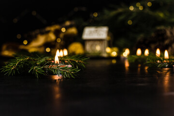 Under the Christmas tree are gifts and small candles are burning. A wooden house and the lights of...