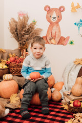 The boy holds an orange pumpkin in his hands. Autumn interior