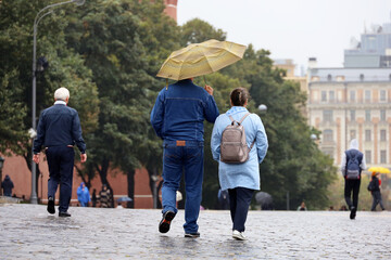 Rain in city, couple with one umbrella walk on a street. Rainy weather in autumn