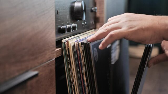 Looking through vinyl records collection at home. Searching for a DJ single or album. Selecting quality music to listen to on a turntable. Background- amplifier. Man hands close-up. Slow motion.