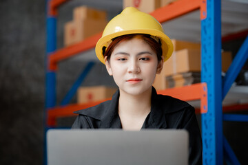 Asian female worker wearing a safety vest is in a warehouse, checking orders and checking balances in a computer system. The concept of working in the warehouse and working in the warehouse is safe.