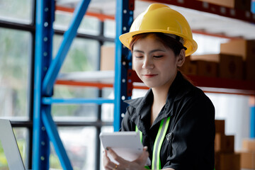 Asian female worker wearing a safety vest is in a warehouse, checking orders and checking balances in a computer system. The concept of working in the warehouse and working in the warehouse is safe.
