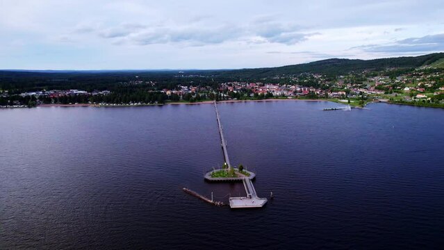 Aerial view during summer's evening. A pier with a peninsula on Lake Siljan in Sweden, people walk on the promenade. View of the beach and the city of Rättvik with red houses, mountains and forests