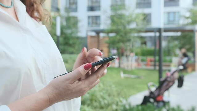 Happy young business woman walking in city street looking into mobile phone smartphone screen chatting online in net smiling answering message in social media using gadget device