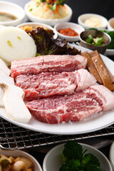 Korean table setting with grilled pork golden brown on the grill and side dishes set 그릴 위 노릇노릇하게 돼지고기를 굽고 있고 반찬이 세팅되어 있는 한상차림