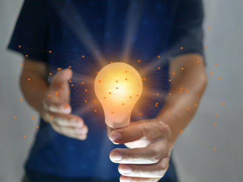 Man holding bright shining light bulb represents a new idea, thought, invention, innovation, solution, creativity, technology, and business with network connection links