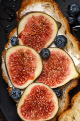 Croissants with cream cheese, figs, blueberries and honey on a black plate. Breakfast concept, top view. Close up, macro photo.
