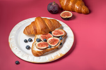 Modern photo on a bright pink background. Croissants with cream cheese, figs, blueberries and honey on a light plate.Breakfast concept, top view. Croissant with healthy dietary filling.