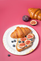 Modern photo on a bright pink background. Croissants with cream cheese, figs, blueberries and honey on a light plate.Breakfast concept, top view. Croissant with healthy dietary filling.