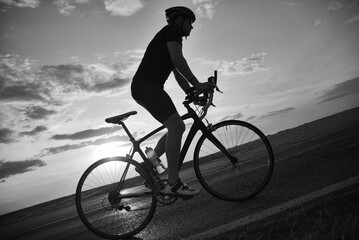 Fototapeta na wymiar Young sports man cycling with bicycle on the road in summer in black and white
