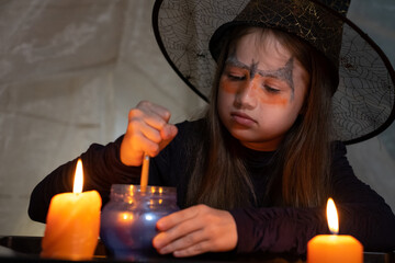 Little witch is making magic potion and reading spell with candle - obrazy, fototapety, plakaty