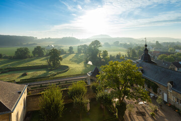 Fototapeta na wymiar Overlooking the medieval chateau Neercanne, which serves as event venue outside Maastricht and a view over the Jeker valley which is covered in layers of mist during an autumn morning after sunrise