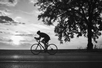 Young sports man cycling with bicycle on the road in summer in black and white