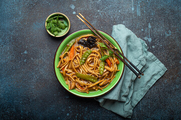 Asian soup with udon noodles, chicken and vegetables in green ceramic bowl with wooden chopsticks...