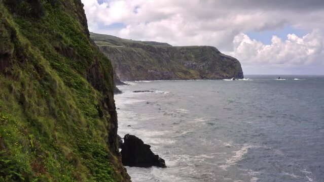 Waves crashing on high rugged coastal cliffs in Azores, flyover shot.