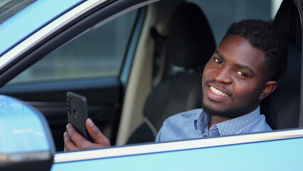 African American driver sitting at car steering wheel talks with friends via videocall. Bearded man...