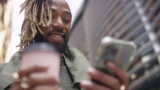 Handsome black man checking his phone and smiling as he sips from a coffee cup, in slow motion