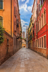 Fototapeta na wymiar Three people walk along a vintage street in Venice on a cloudy summer morning, sunlight on a stone Venetian road, old brick walls of warm colors in Venice