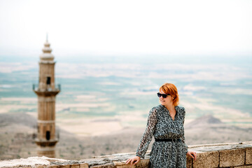 Woman in sunglasses standing in Mardin, Turkey in front of mosque and Mesapotamian valley.