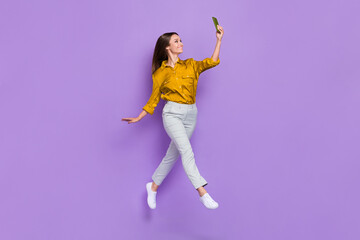 Full size photo of energetic cheerful girl jump hold telephone take selfie isolated on violet color background