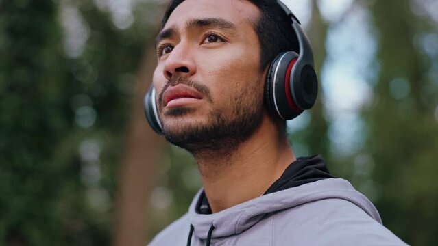 Tired, man runner and headphones listening to music, breathe hard and training for running marathon in outdoor park. Fitness, workout and exercise young healthy Asian sports athlete outside in nature
