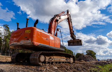 A large orange crawler excavator against a blue cloudy sky