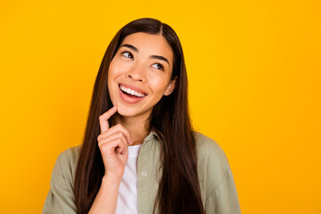 Portrait of creative minded girl toothy smile finger touch chin look empty space isolated on yellow...