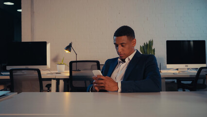 African american businessman in suit using cellphone in office at night.