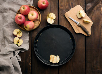 Empty round non-stick baking sheet, fresh apples on a wooden brown table