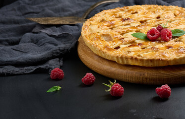 Round baked apple pie on a black table.