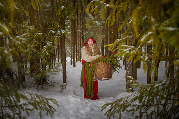 Little girl in old peasant clothes including a fur coat and a shawl in a cold winter forest with...