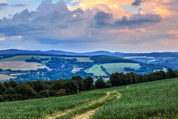 Fototapeta na wymiar Rural landscape with path in the field at sunset. Beautiful sky with colorful clouds. View from above into the valley. Horna Suca, Slovakia.