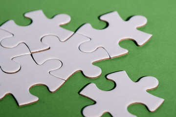 Close-up on jigsaw puzzle pieces, blank white paper jigsaw puzzle elements linked together and separate. Closeup shot on green paper. Abstract background metaphor on teamwork challenge, togetherness.