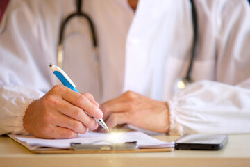 Close up Doctor writing notes while working on a computer in a medical office
