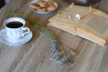 Cup of tea, plate with chocolate chip cookies, open book, reading glasses, lit candles and dry lavender flowers. Hygge at home, selective focus.