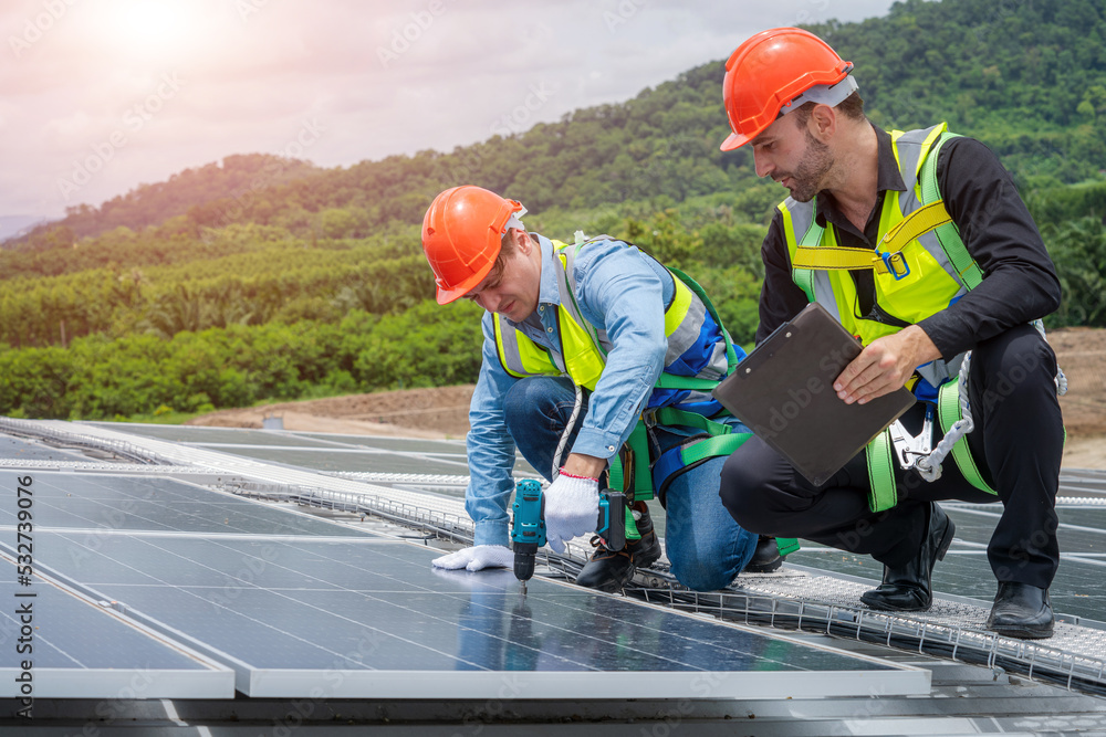 Poster technician wearing safety harness belt using drill during installing the solar panels on roof struct