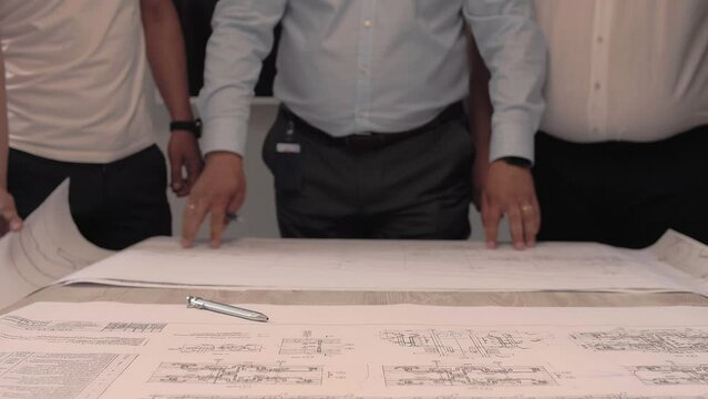 Team of professional engineers reveals a huge sheet with the technical design plan of the engineering structure. 