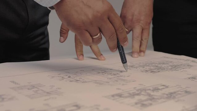 Design engineers are discussing a complex technical diagram drawn on a large sheet of paper. Close-up 
